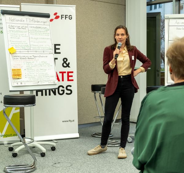 Eine Frau erklärt den Zuhörer:innen die Texte auf einem Flipchart
