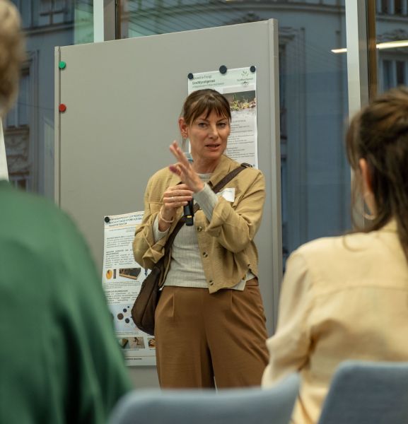 Eine Frau erklärt den Zuhörer:innen die Texte auf einem Flipchart